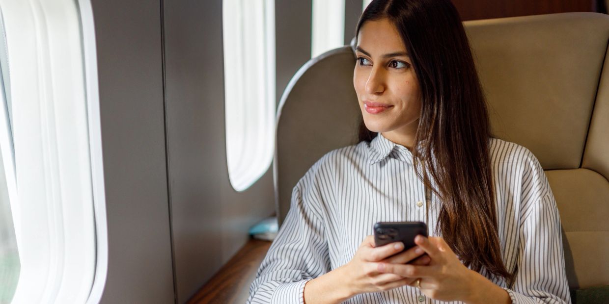 Woman holding a phone, looking out an airplane window thoughtfully.