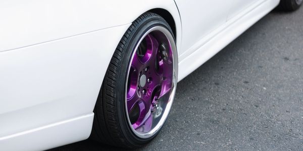 Car wheel with purple rim on a white car.