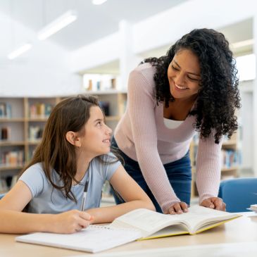 Teacher helping student with her studies in a library.