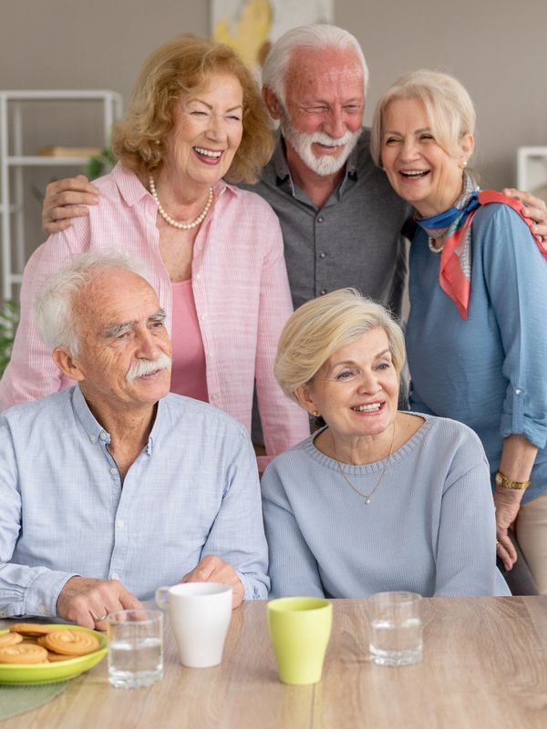 Six elderly friends happily taking a selfie together at a dining table at the assisted living and memory care community.