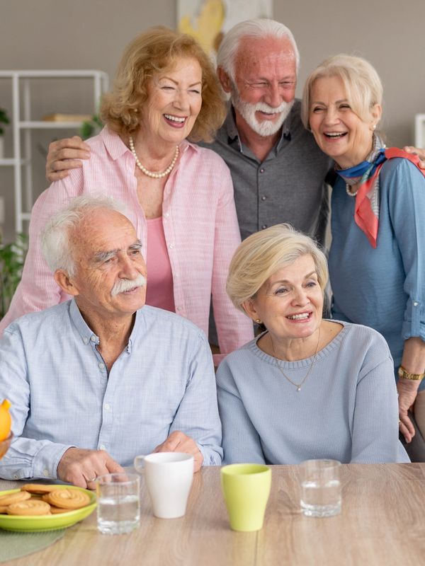 Six elderly friends happily taking a selfie together at a dining table at the assisted living and memory care community.