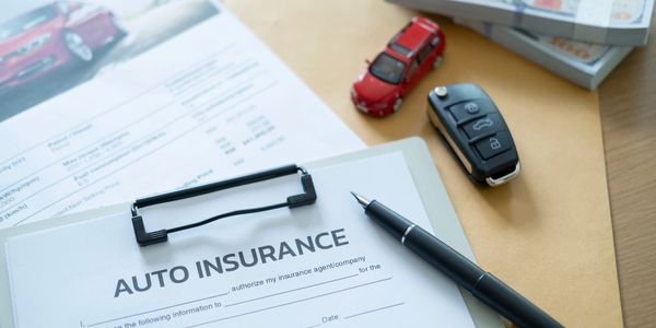 Auto insurance form with pen, car key, and toy car on desk.