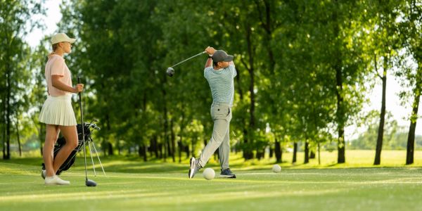 Man swinging golf club while woman watches on a golf course.