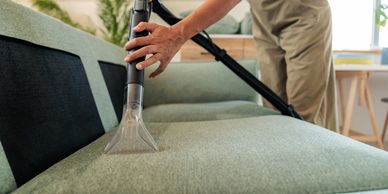 Person cleaning couch with vacuum upholstery tool.
