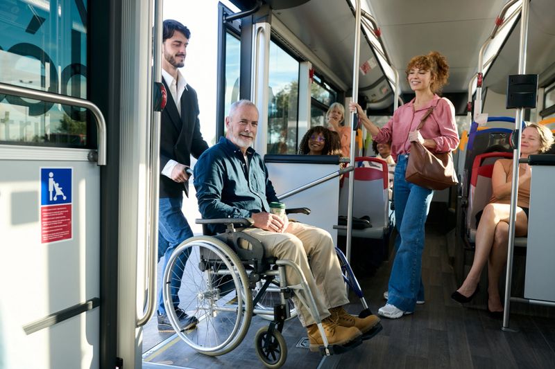 Young man assisting a smiling senior adult in a wheelchair entering a modern public bus, promoting accessibility, diversity, and urban transport