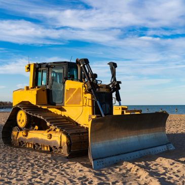 Yellow bulldozer on sandy beach under blue sky.