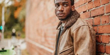 Man leaning against brick wall looking serious.