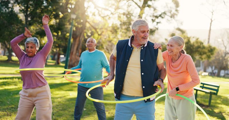 Senior people, group and exercise with hoop at park for active retirement, health or laugh. Elderly friends, ring and fitness outdoor, funny joke or workout for balance at wellness class for cardio