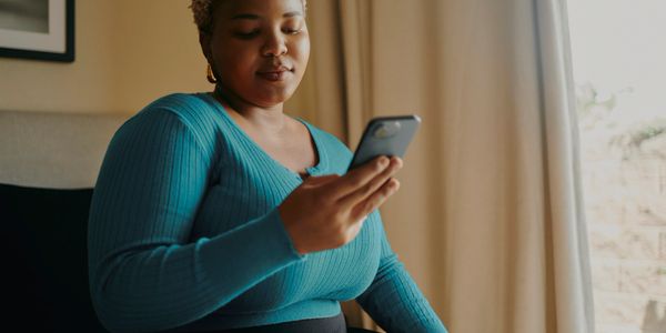 Woman in teal sweater looking at her phone indoors.