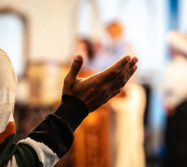 A person raising a hand in a gesture of prayer or worship indoors.