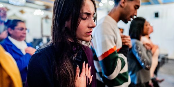 People praying with eyes closed and hands on chest.