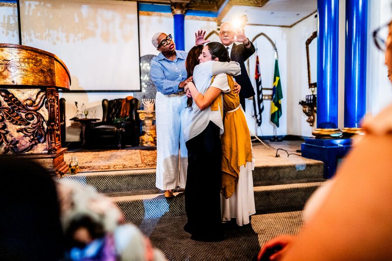 A deeply emotional moment captures two church members embracing warmly, surrounded by the interior of a church sanctuary. The intimate interaction reflects a sense of community, support, and spiritual connection, with blue and warm-toned lighting creating a compassionate atmosphere.