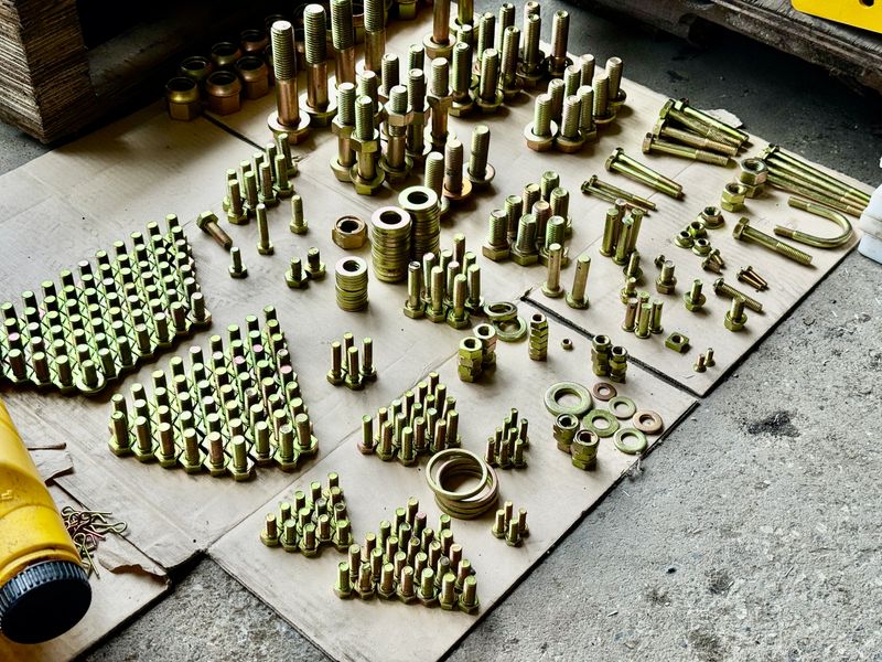 Assorted bolts, nuts, washers, and fasteners neatly arranged on cardboard, showcasing organized industrial hardware in a workshop setting.