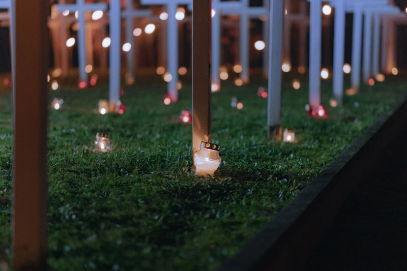 Candle Burning by White Cross at Night Memorial Cemetery