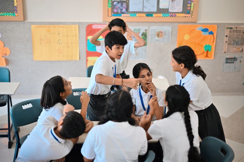 A lively group of middle school students gathers around a desk during recess, laughing, pointing, and animatedly chatting. The playful scene captures friendship, teen conversation, and carefree “timepass” between classes—ideal for themes of youth, social interaction, school life, and group dynamics.