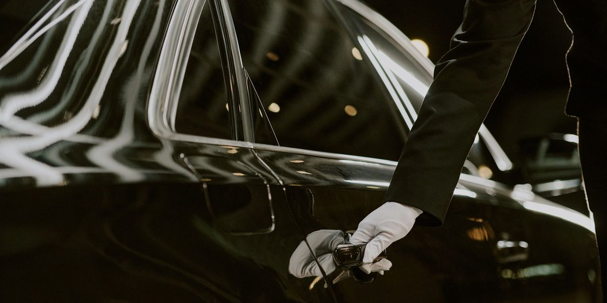 Gloved hand opening a sleek black car door.