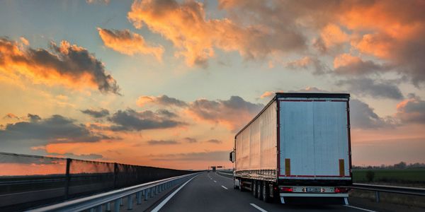 A truck driving on a highway during a colorful sunset.