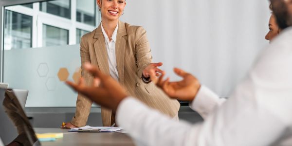 Businesswoman smiling while talking to colleague at office desk.