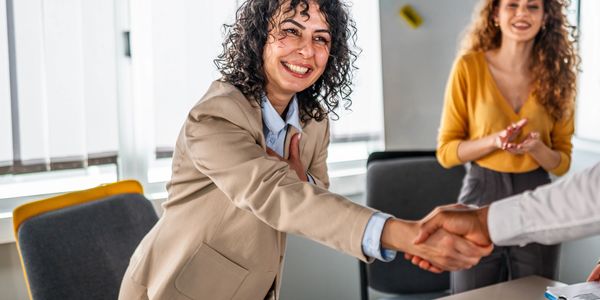 Businesswoman smiling and shaking hands in an office setting.
