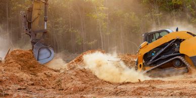 Excavator and bulldozer working on dusty soil.