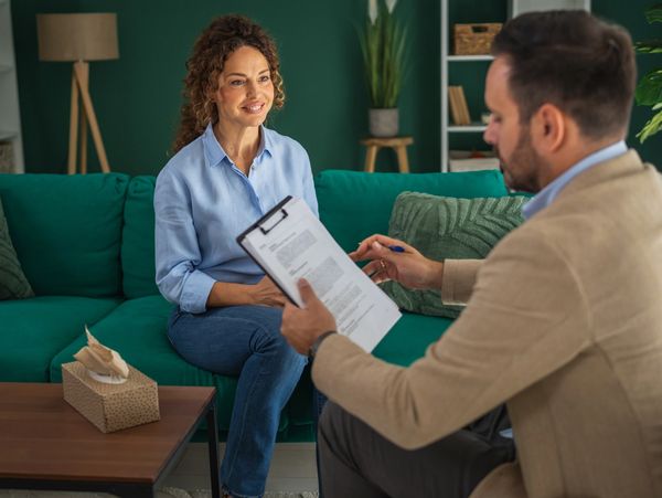 A woman sitting on a couch during a therapy session with a male therapist.