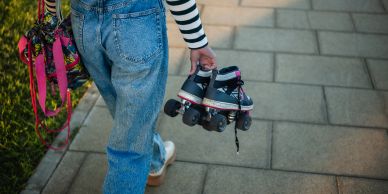 Person holding roller skates and leashes while walking on pavement.