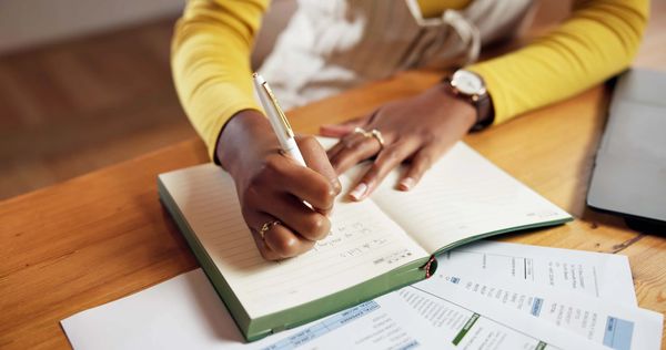 Person writing in a notebook with financial documents nearby.