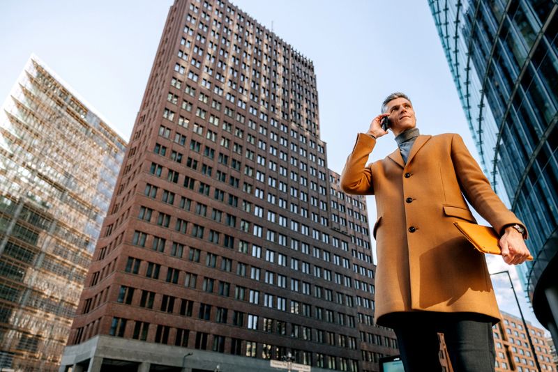 A confident mature man in stylish business attire walks through a busy urban street while talking on his smartphone. Captures a modern professional lifestyle in the city environment