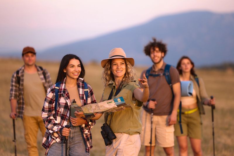 Happy park ranger showing her tourist where to go on hiking in a meadow. Copy space.