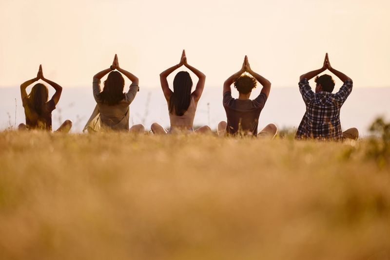 Rear view of group of friends doing Yoga meditation exercises with their hands clasped above their heads during springtime in a meadow. Copy space.