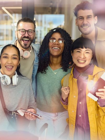 A joyful group of five diverse friends smiling and posing together indoors.