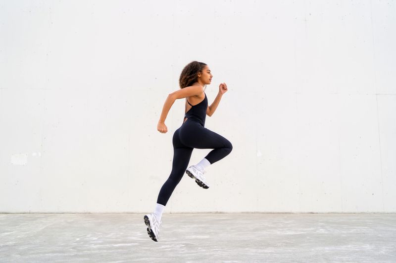 Young athletic woman mid-jump running along urban concrete wall, showcasing energy, strength and healthy active lifestyle in motion