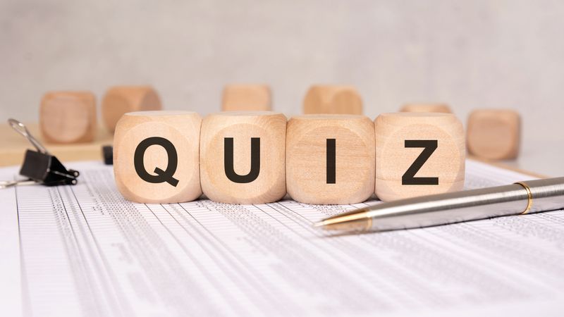 Close-up of wooden cubes spelling QUIZ on office desk with pen and documents, symbolizing knowledge test, learning, survey, or education concept in a neutral workspace