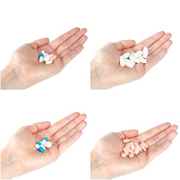 Four hands holding different types of pills and capsules.