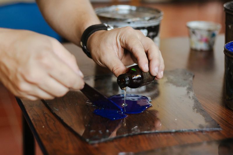 Artist carefully pouring solvent into concentrated blue ink for printmaking, preparing materials on a mixing plate in a studio