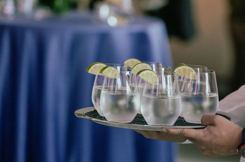 Refreshingly chilled water in stemless glasses, each garnished with a lime wedge and served on a metal tray at a formal event. Ideal for hospitality, catering, and social gatherings.