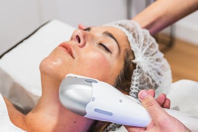 Woman receiving a facial treatment with a handheld device.