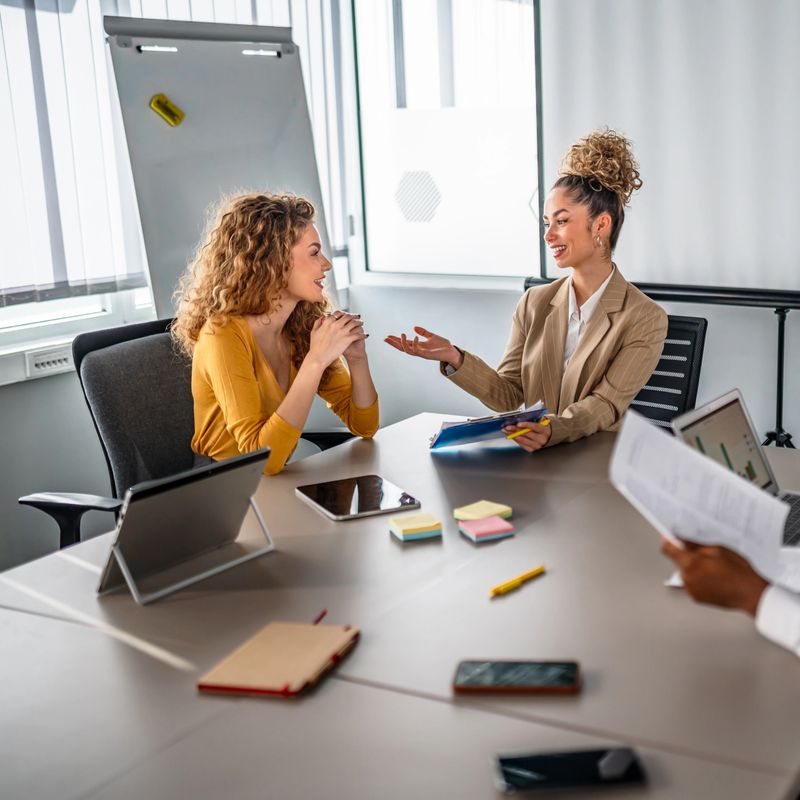 Two businesswomen collaborating and sharing ideas during a casual discussion in a modern office conference room