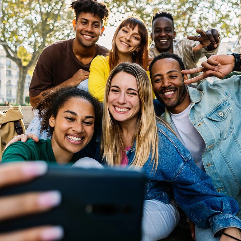 Multiracial young happy group of student friends taking selfie portrait together using mobile phone outdoors