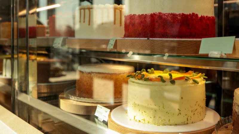 A variety of cakes are showcased in a glass display case, enticing customers with their delicious appearance