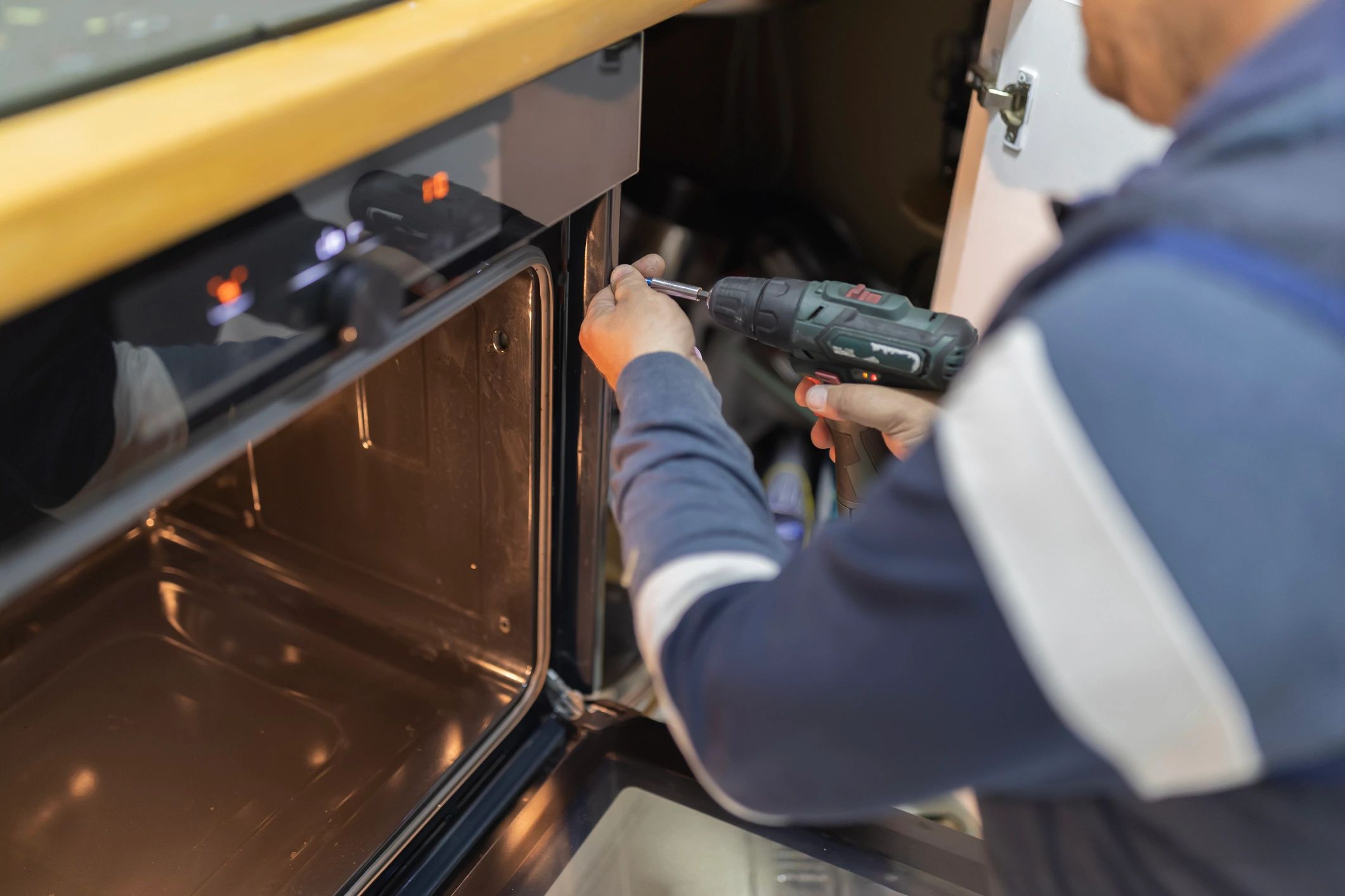 Person fixing an oven with a power drill.