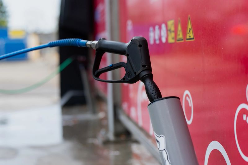 High pressure water wash nozzle with blue hose positioned beside red equipment panel, showing mobile car washing system setup, spray connection point and operational service configuration