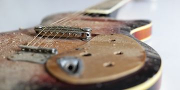 Close-up of a dusty, worn electric guitar.