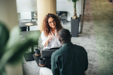 Two colleagues discussing work at a table with coffee.
