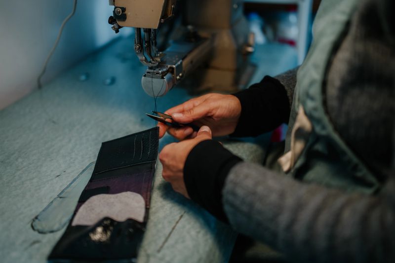 Artisan's hands carefully sewing a leather wallet with a powerful industrial sewing machine, creating a handmade product