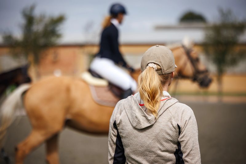 Horse trainer closely monitoring rider preparing for dressage event. Horseback riding in equestrian paddock