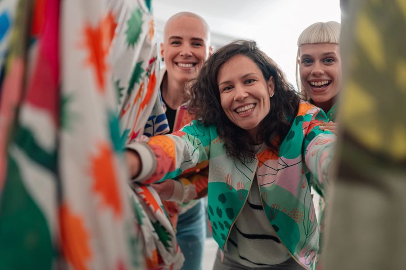 Three happy young adult women comparing new patterned jackets while smiling in a modern fashion store