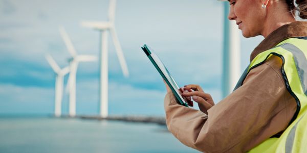 Engineer inspecting wind turbines using a tablet by the sea.
