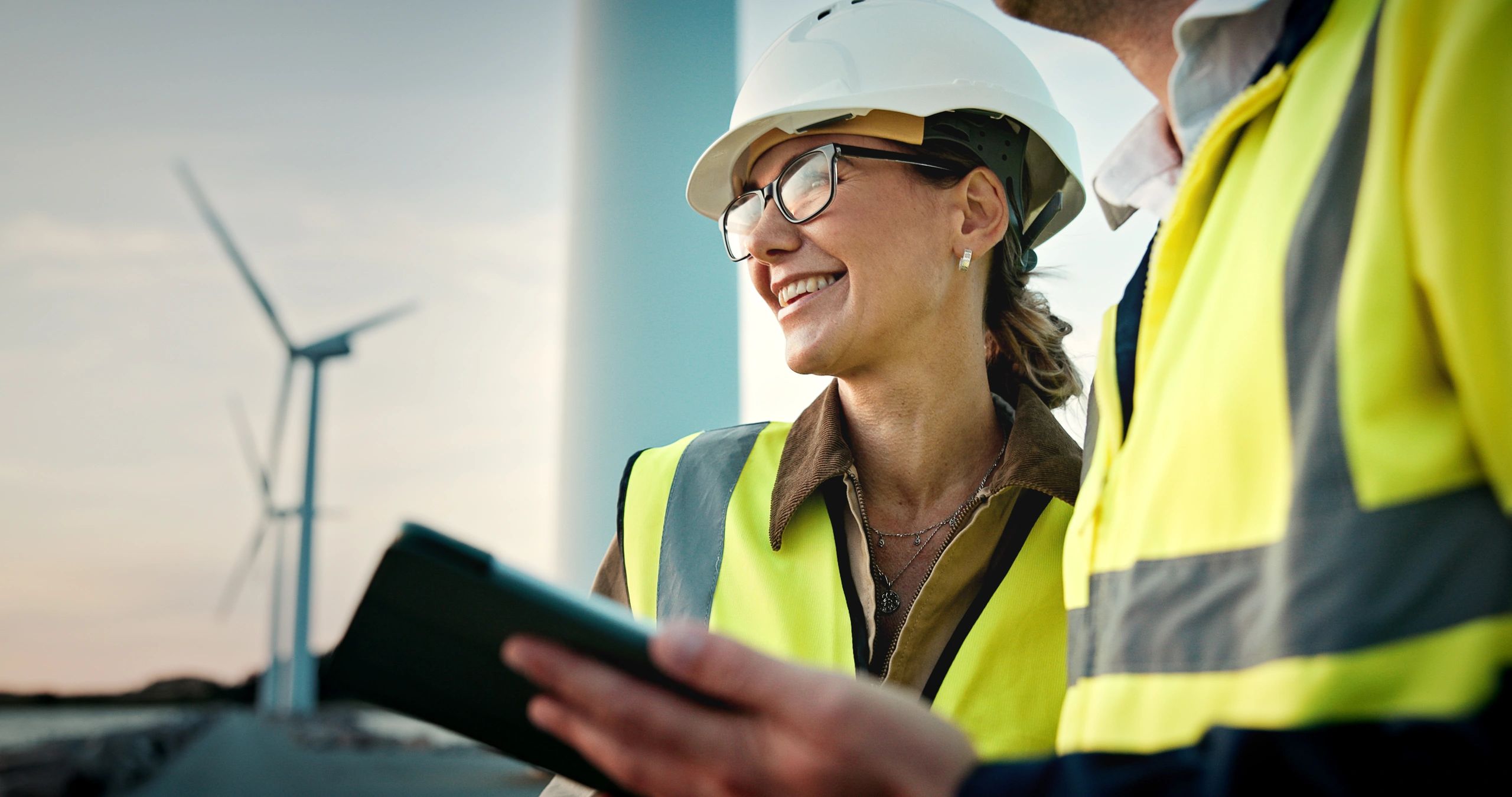Two engineers in safety gear at a wind farm.