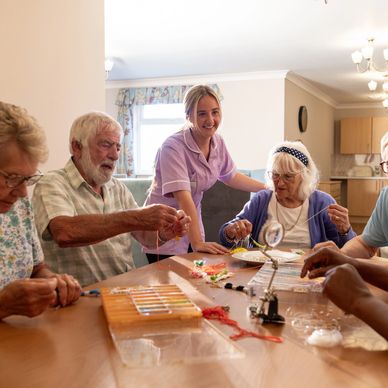 A group of residents are enjoying a craft activity, seated together at a table